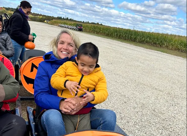 A therapist holding a young student outdoors on a fall farm visit